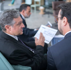 Multiple people in business attire sitting at a conference table. Two in the foreground are discussing a paper held by one.