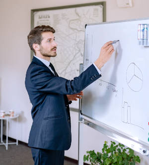 A person in business attire writing on a standing whiteboard.